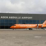 An orange aircraft parked in front of Aden Abdulle Airport with glass windows.